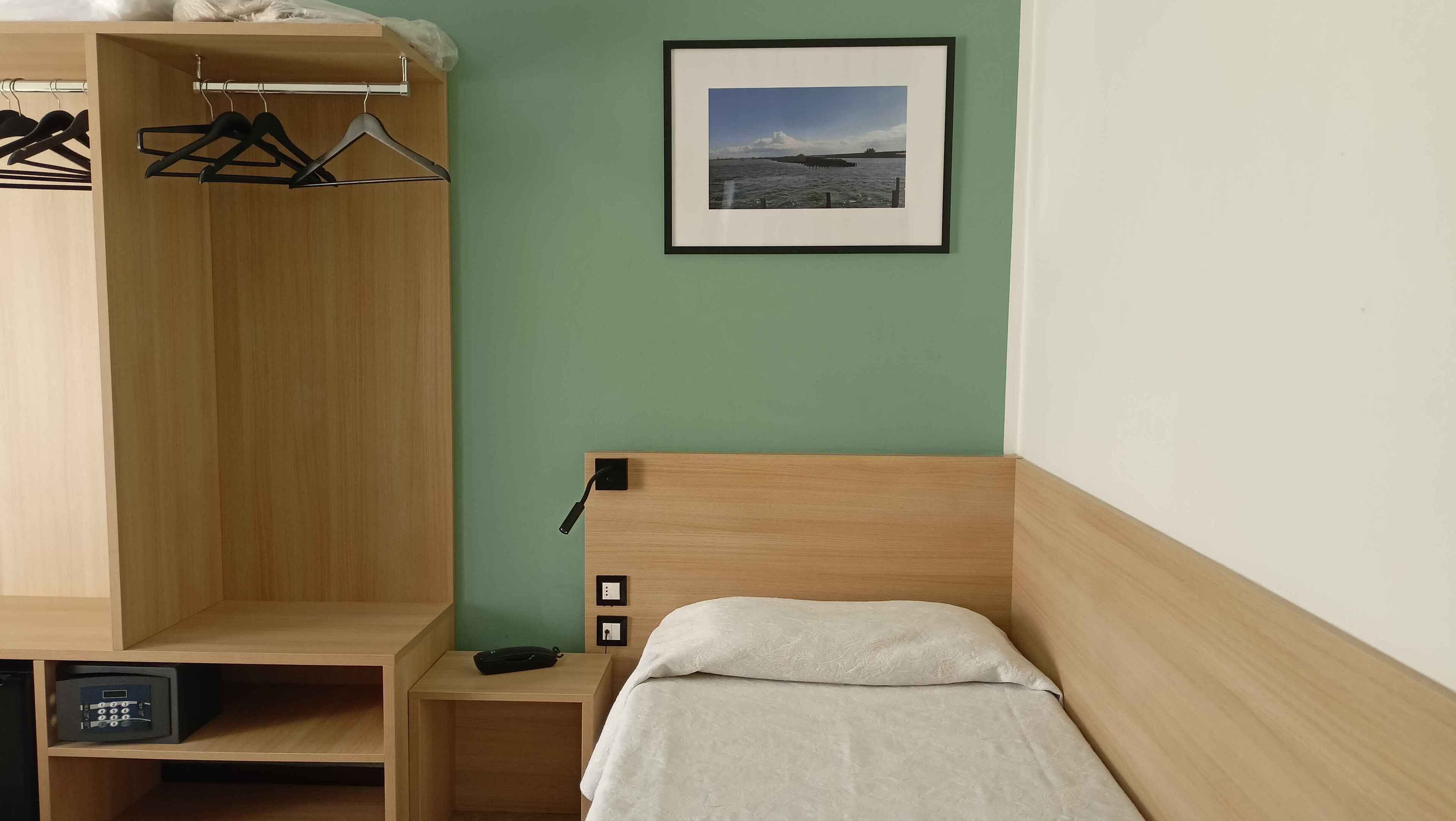 A bedroom with a bed, a wooden wardrobe, a nightstand, and a framed picture on the wall.