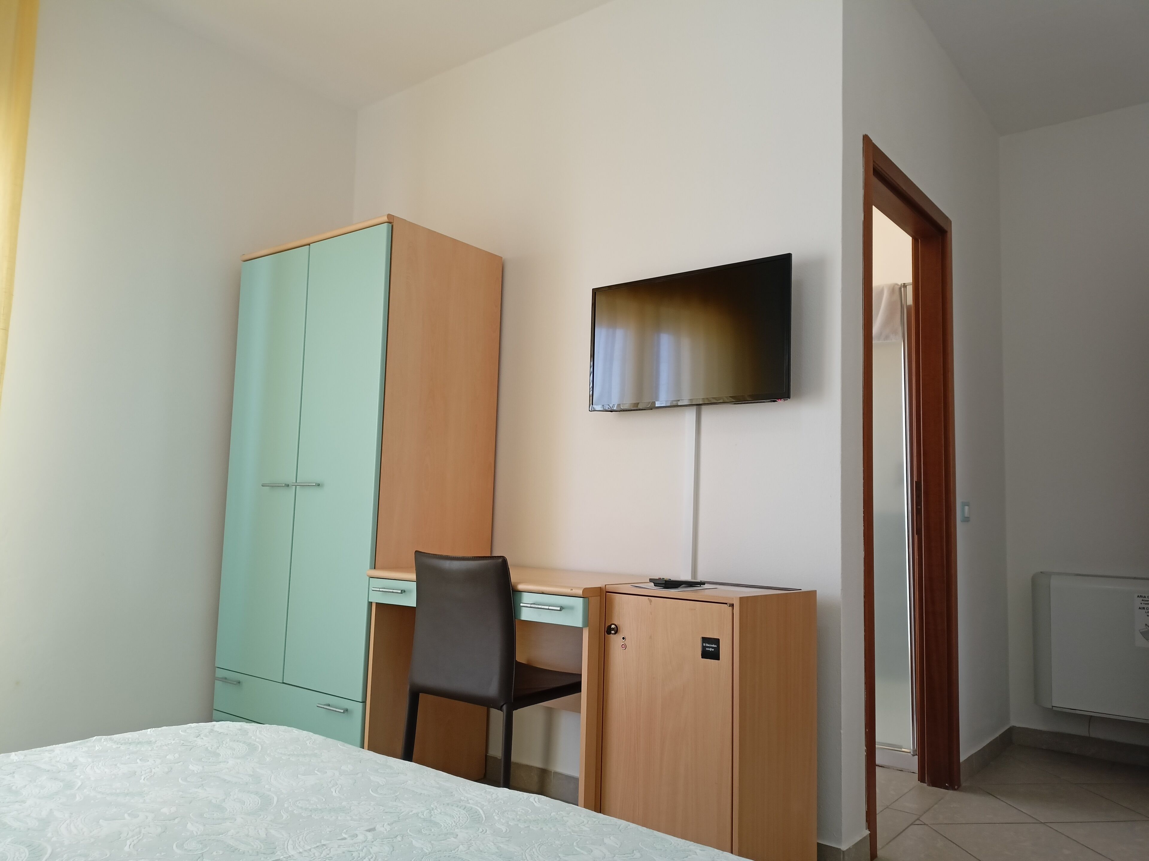 Een slaapkamer met een bed, een bureau, een stoel, een kledingkast, een televisie en een radiator.