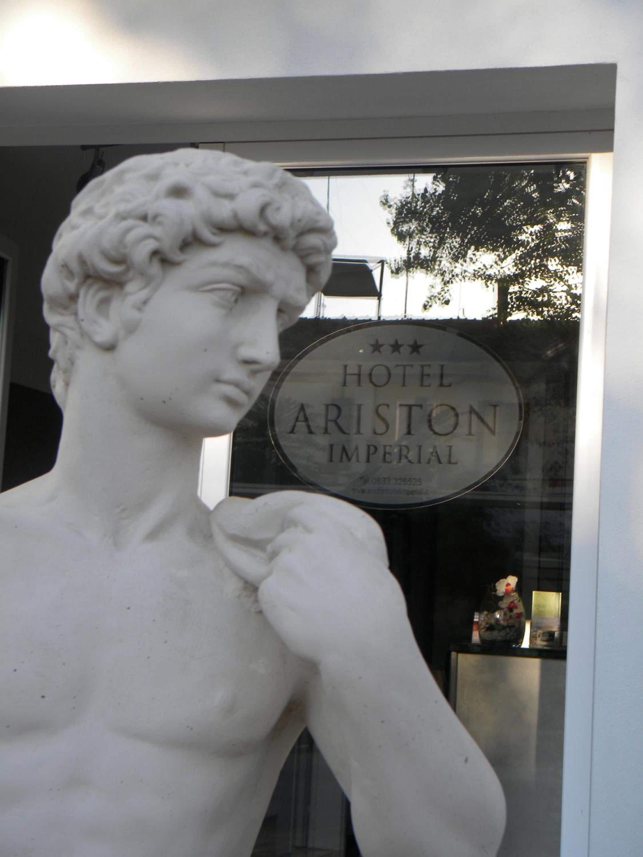 A statue of a classical figure in front of a hotel sign.