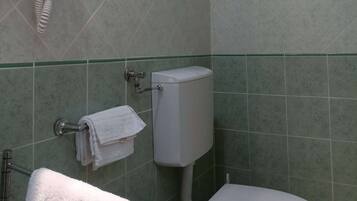A bathroom with a toilet, a towel rack, and a hairdryer on a wall socket.
