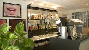 Een barruimte met drankflessen op planken, een koffieapparaat en een groot raam met jaloezieën.