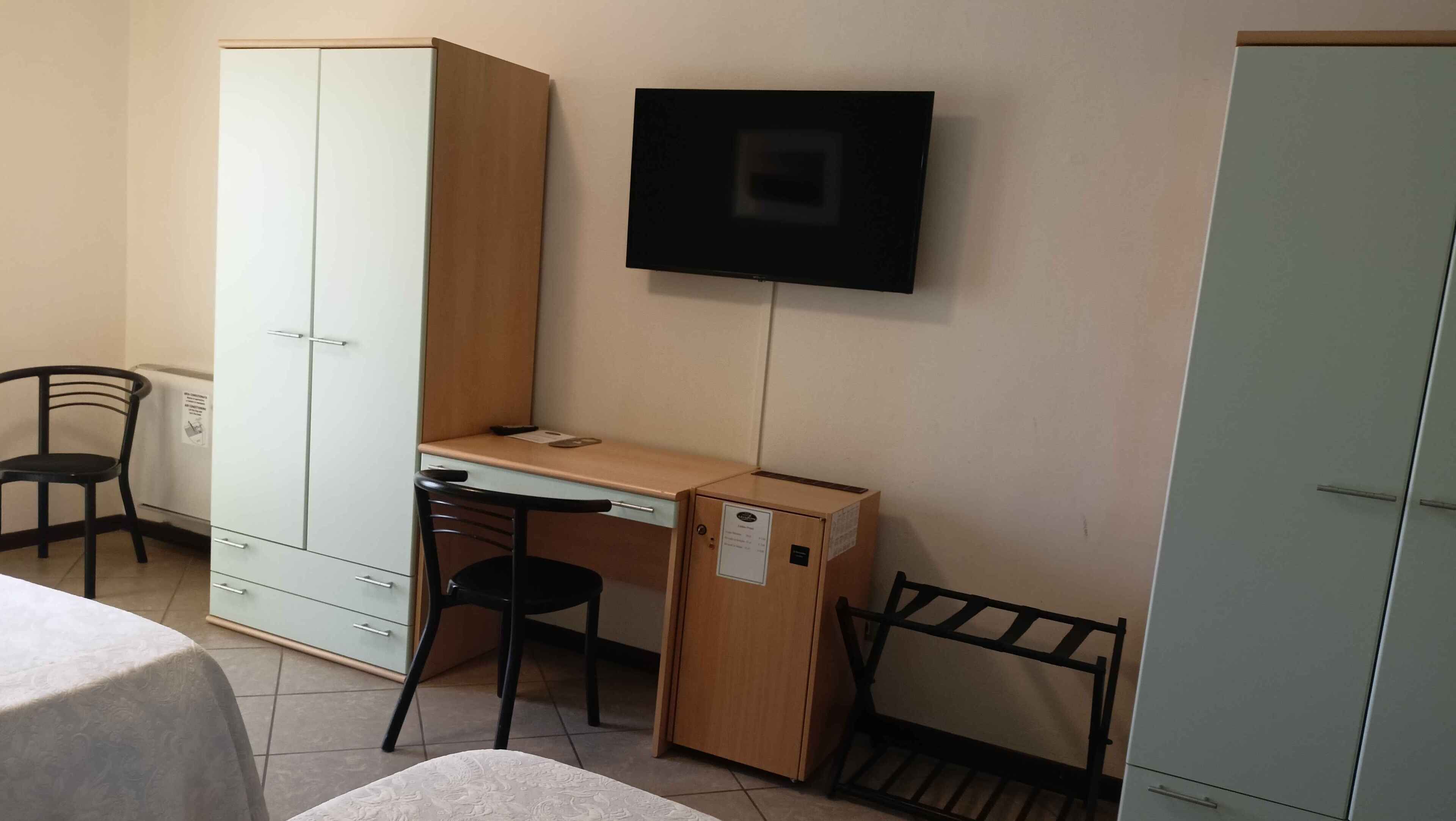 A small room with a bed, a desk, a chair, a wardrobe, and a television.