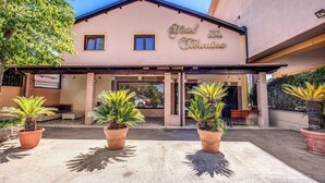 A hotel entrance with a sign reading "Hotel Tiburina," featuring a covered patio area with potted plants and a bench. - Hotel Roma Tiburtina (Rome)