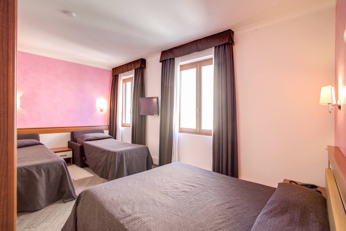 Ett hotellrum med två separata sängar, en tv och ett fönster med gardiner.
