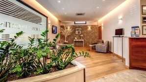 A reception area with a wooden reception desk, a seating area with chairs, and a large potted plant. - Hotel Roma Tiburtina (Rome)