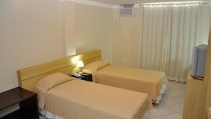 Habitación de hotel con dos camas individuales, una mesita de noche con lámpara, televisión y ventana con cortinas.
