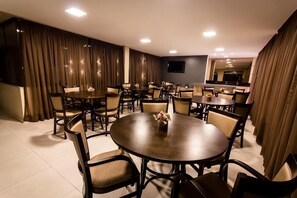 A conference room with multiple tables and chairs, a flat-screen TV mounted on the wall, and a large window with curtains. - Marc Center Hotel (Campina Grande)