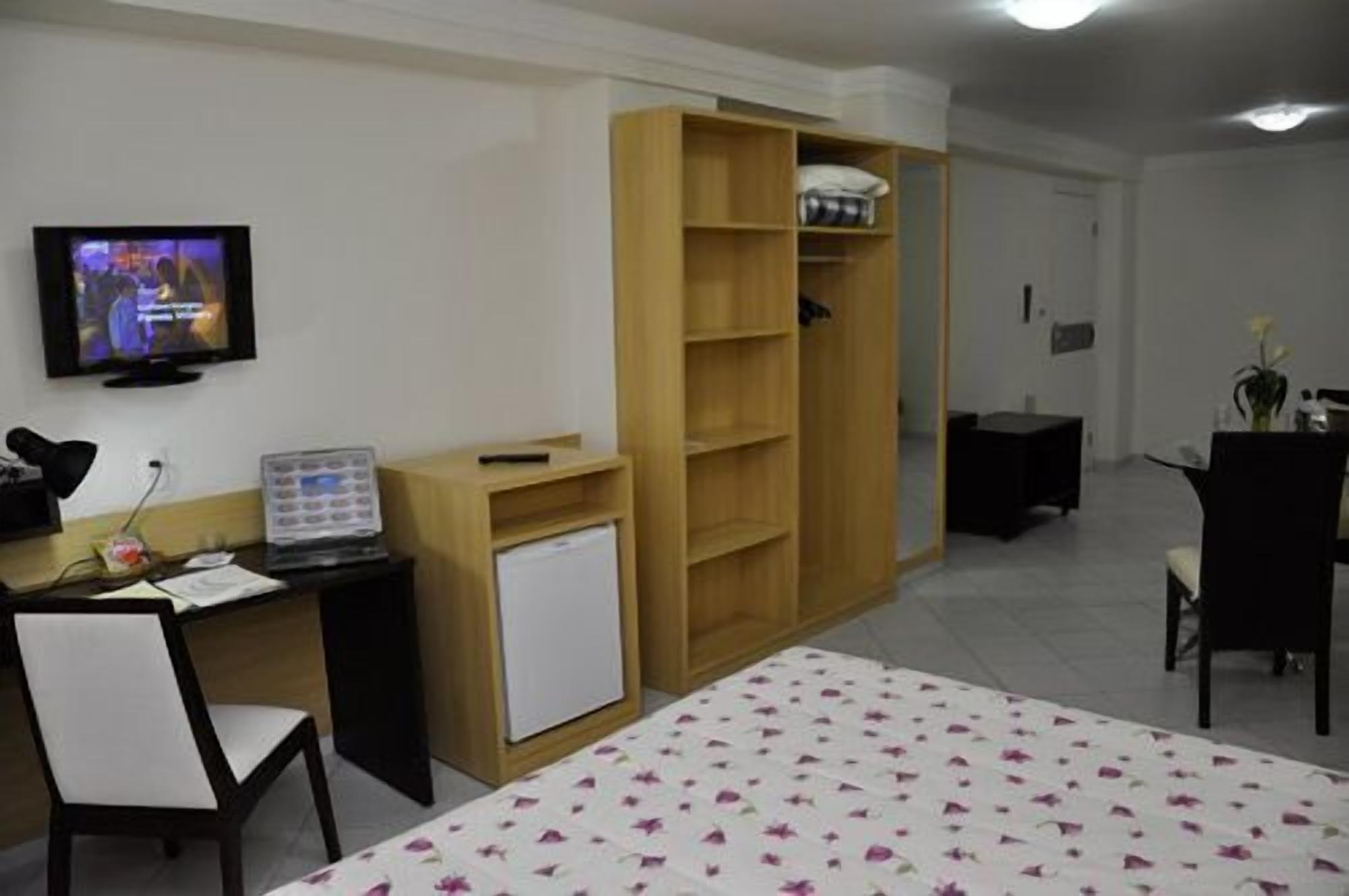 A hotel room with a bed, a desk with a computer, a television, and a wardrobe.