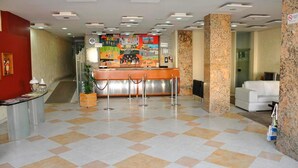 Un área de recepción con mostrador de entrada, una pared roja, suelo de baldosas y un sofá blanco al fondo.