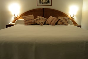 Un lit bien fait, avec une tête de lit en bois, plusieurs oreillers et des lampes de chevet.