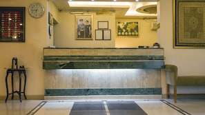 A reception desk with a clock, framed certificates, and a world map. - Aghadeer Hotel (Amman)