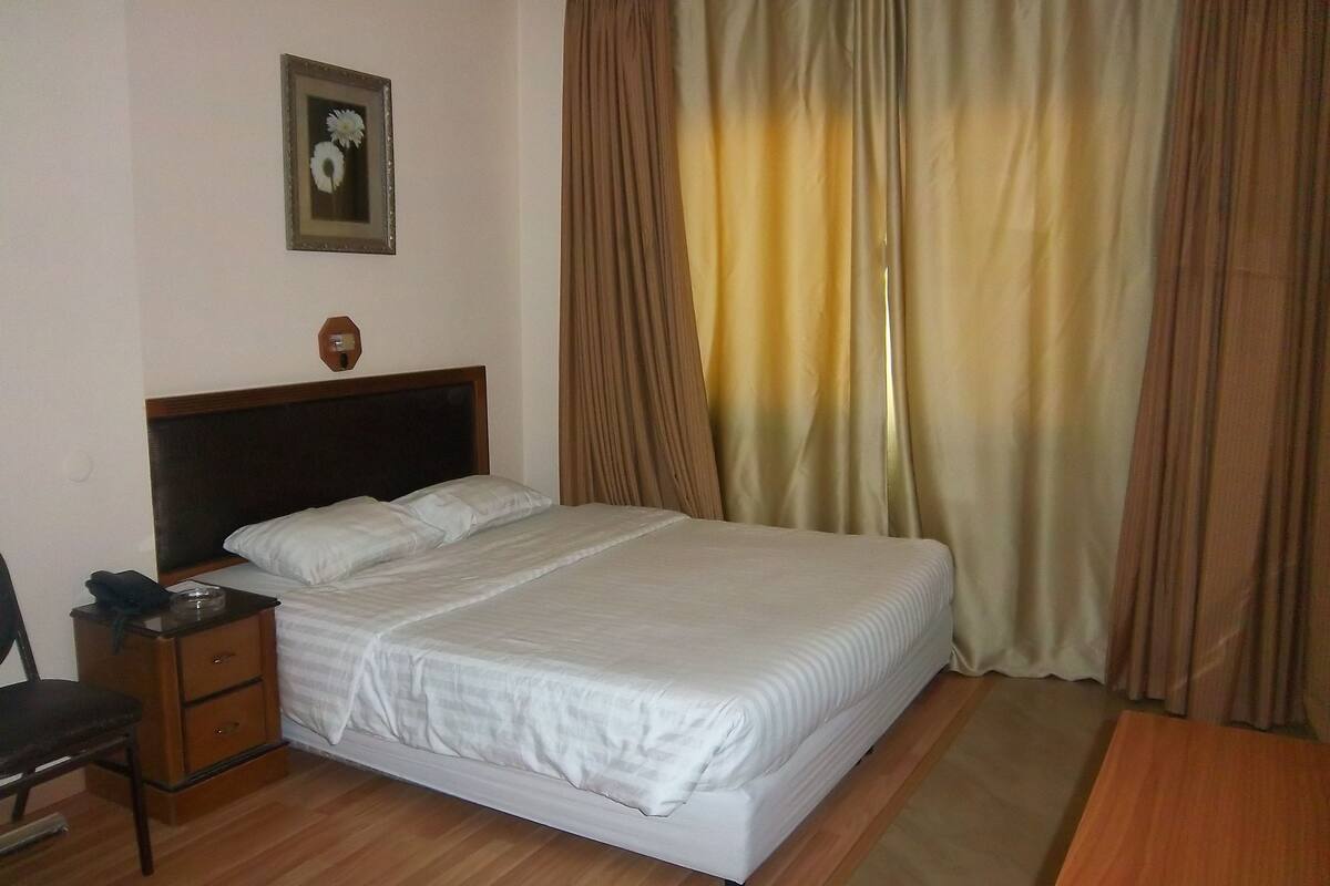 A neatly made bed with a wooden headboard, a bedside table with a lamp, and a chair.