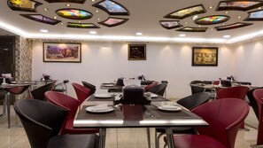 A dining area with tables set for four, red and black chairs, and ceiling artwork. - Aghadeer Hotel (Amman)