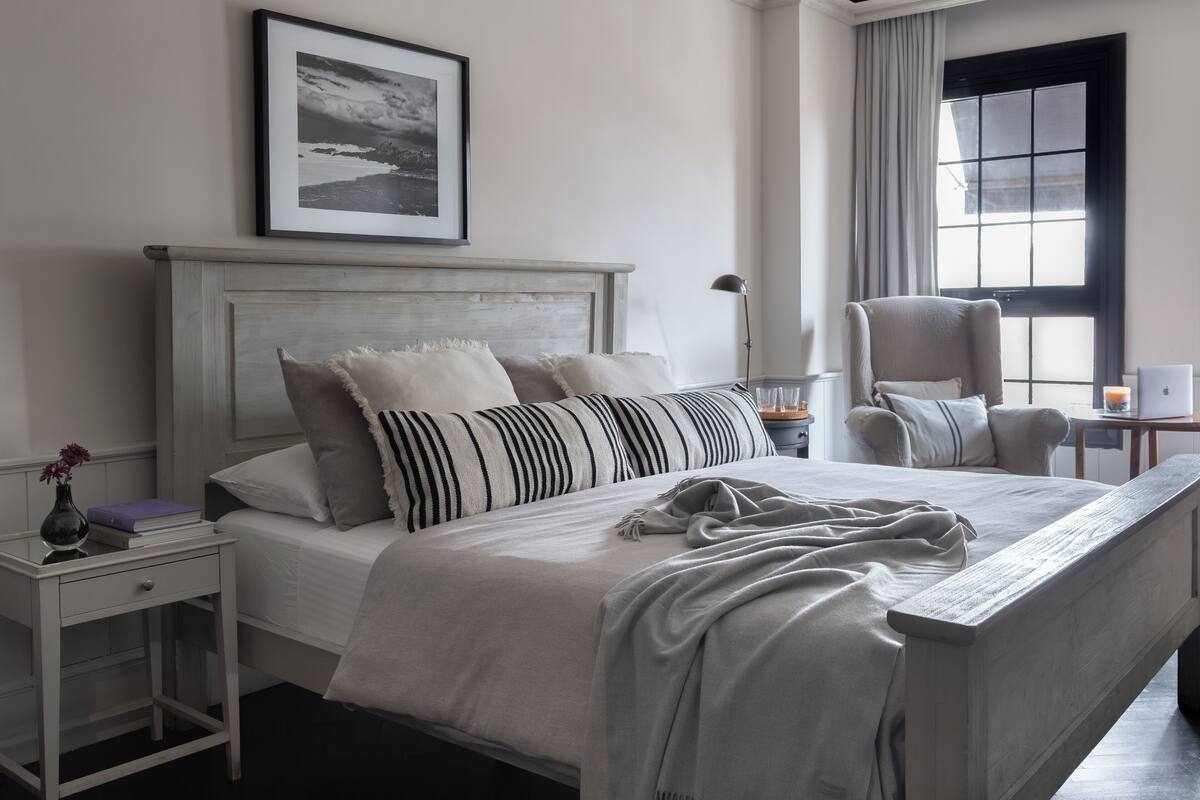 Une chambre bien rangée, avec un lit, des tables de chevet, une chaise et une fenêtre avec des rideaux.
