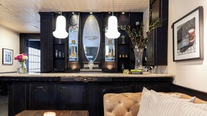 Un espace bar aux couleurs sombres, agrémenté d’un grand miroir, de luminaires suspendus et d’un canapé avec des coussins à rayures.