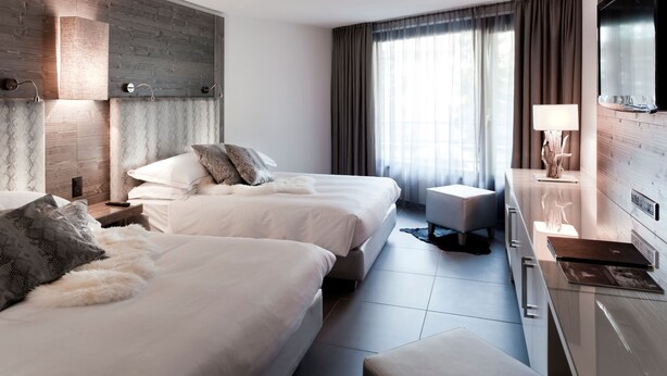 A modern hotel room with two beds, a desk, and a TV.