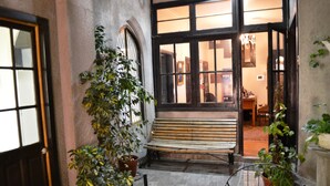 A courtyard with a bench, potted plants, and a view into a room with a chandelier. - Landay Hostel (Santiago)