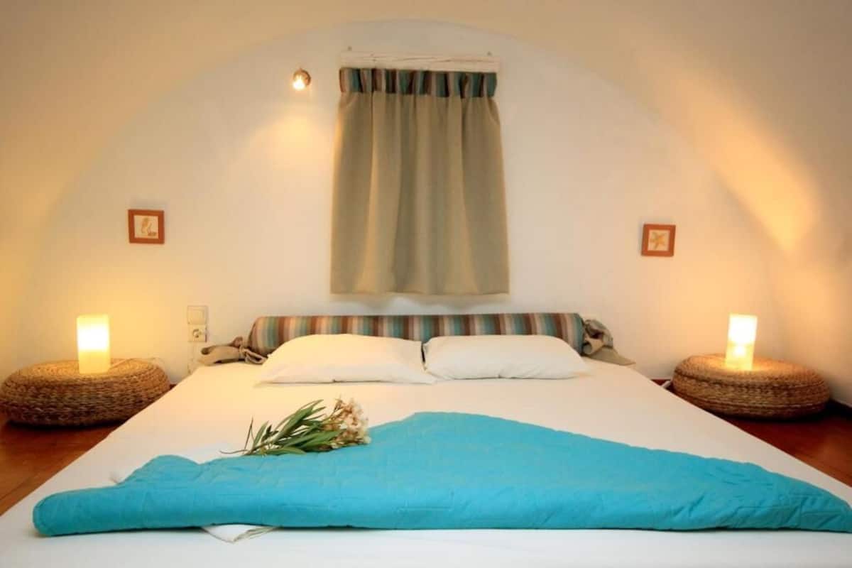 Ein ordentlich bezogenes Bett mit einer blauen Decke, zwei Nachttischlampen und einem Vorhang.
