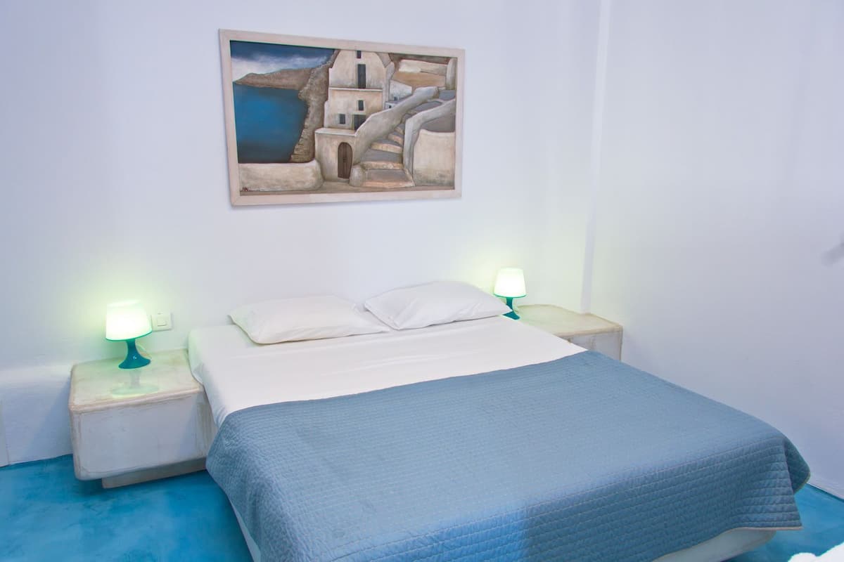 Ein Schlafzimmer mit einem Bett, zwei Nachttischen mit Lampen, einem Bild an der Wand und einem blauen Boden.