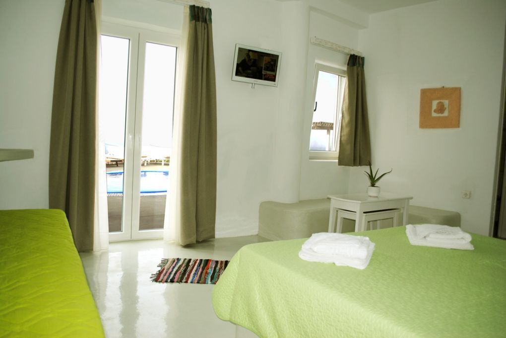 Habitación de hotel con cama, escritorio, silla, una mesita con planta y ventana con cortinas.