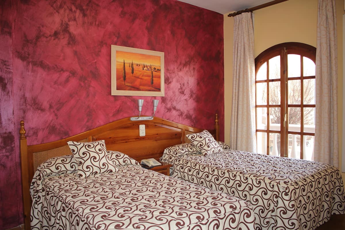 A bedroom with a wooden bed, patterned bedding, a painting on the wall, and a window with curtains.