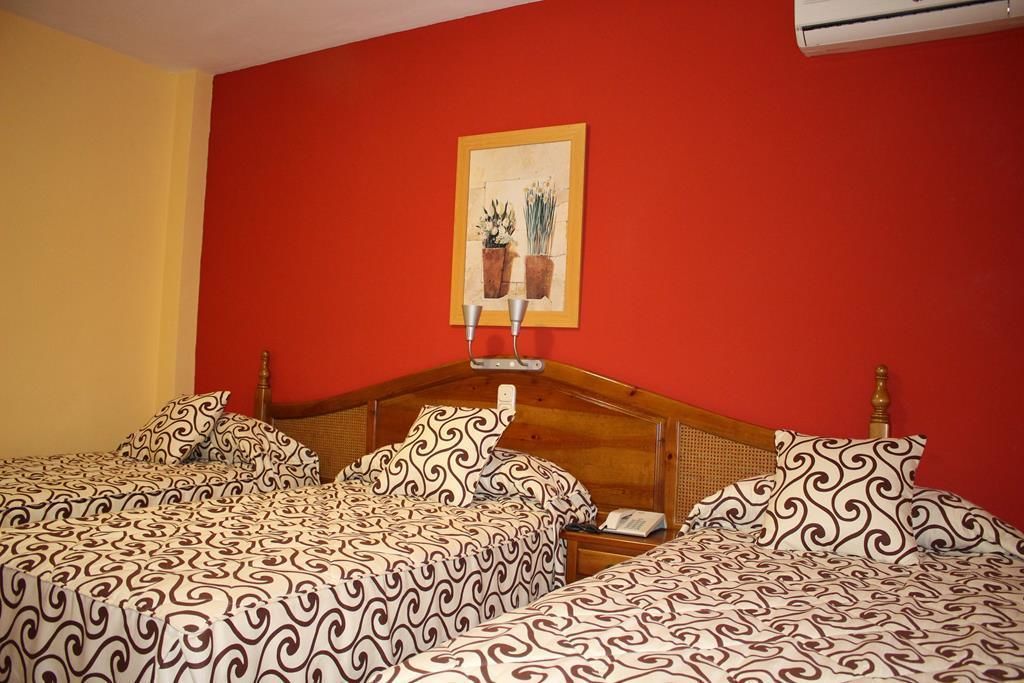 Une chambre d’hôtel avec un mur rouge, une tête de lit en bois et deux lits avec une literie à motifs.
