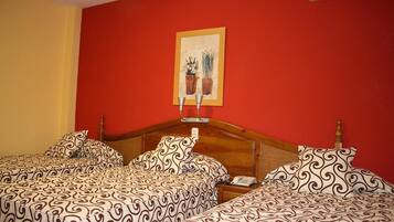 Une chambre d’hôtel avec un mur rouge, une tête de lit en bois et deux lits avec une literie à motifs.