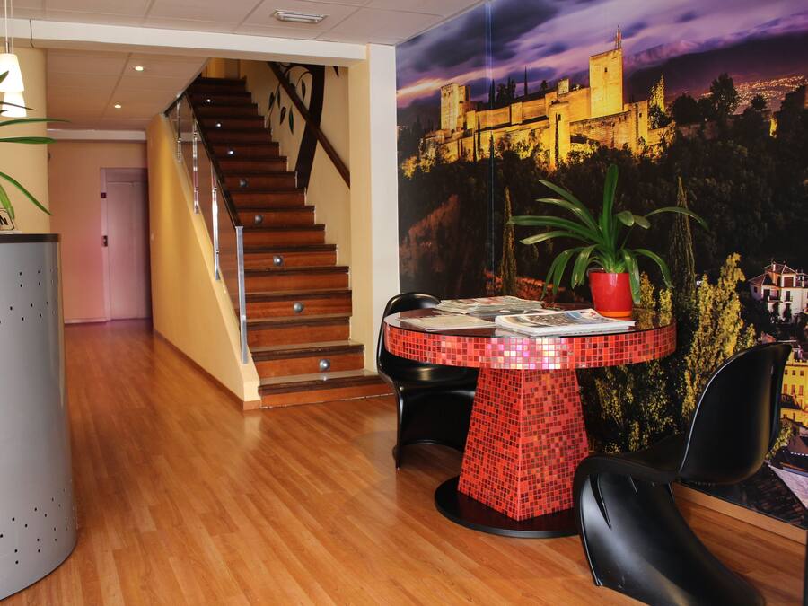 Zona de recepción con mostrador, escalera y mesa de comedor con sillas.