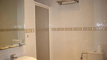 Un baño con lavamanos blanco, espejo e inodoro. Hay una repisa de vidrio sobre el lavamanos y un perchero encima del inodoro.