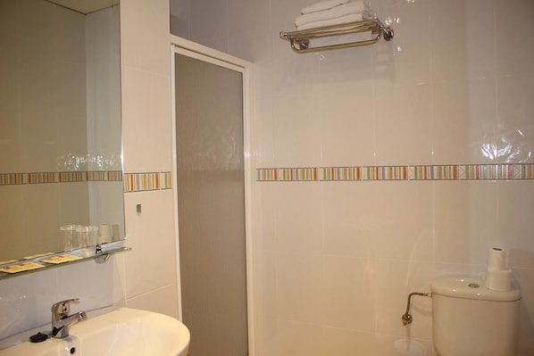 A bathroom with a white sink, mirror, and toilet. There is a glass shelf above the sink and a towel rack above the toilet. - Hotel La Curva (Albolote)