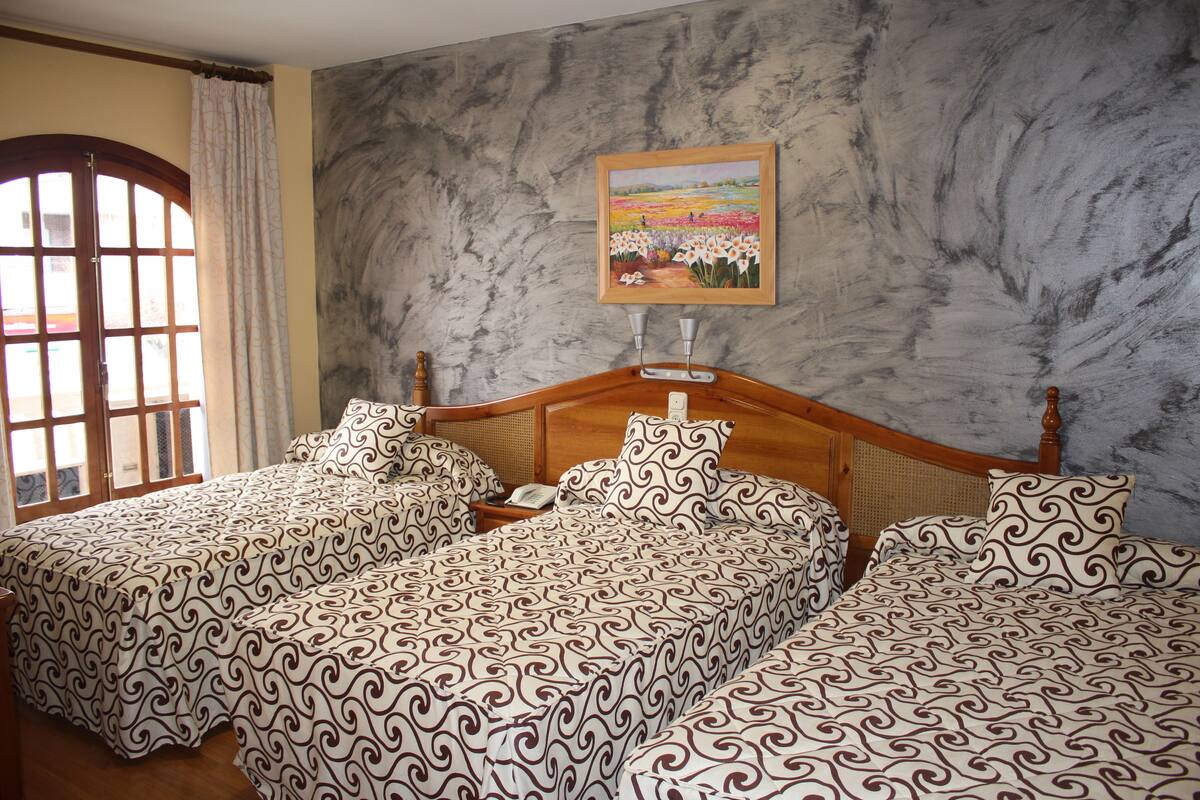 A hotel room with two beds, a wooden headboard, a painting on the wall, and a window with curtains.