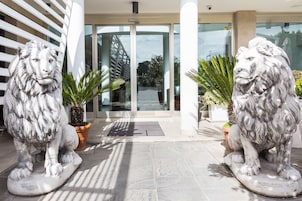 Due statue di leoni in pietra davanti all'ingresso di un edificio con porte in vetro e piante in vaso.