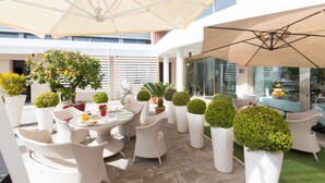 A rooftop patio with outdoor seating, potted plants, and a glass enclosure. - JC Hotel (Rome)