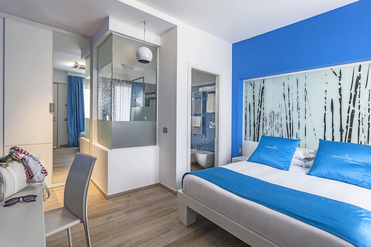 A modern hotel room with a large bed, a desk, and a bathroom visible through an open door.