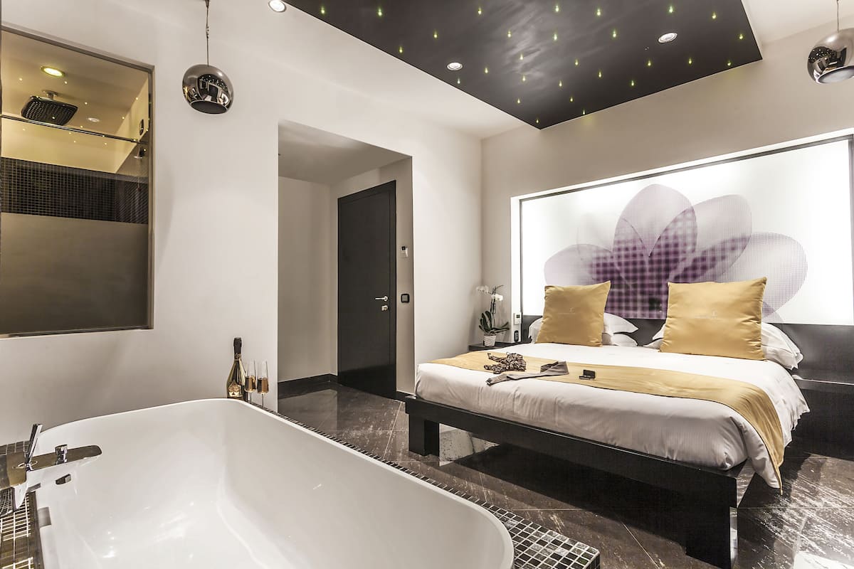 A modern bedroom with a large bed, a bathtub, and a large window with a flower design.