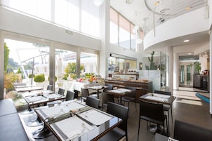 En moderne restaurant med høje lofter, store vinduer og forskellige siddepladser.