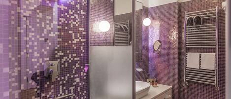 A bathroom with purple mosaic tiles, a glass shower enclosure, a sink, and a bidet.