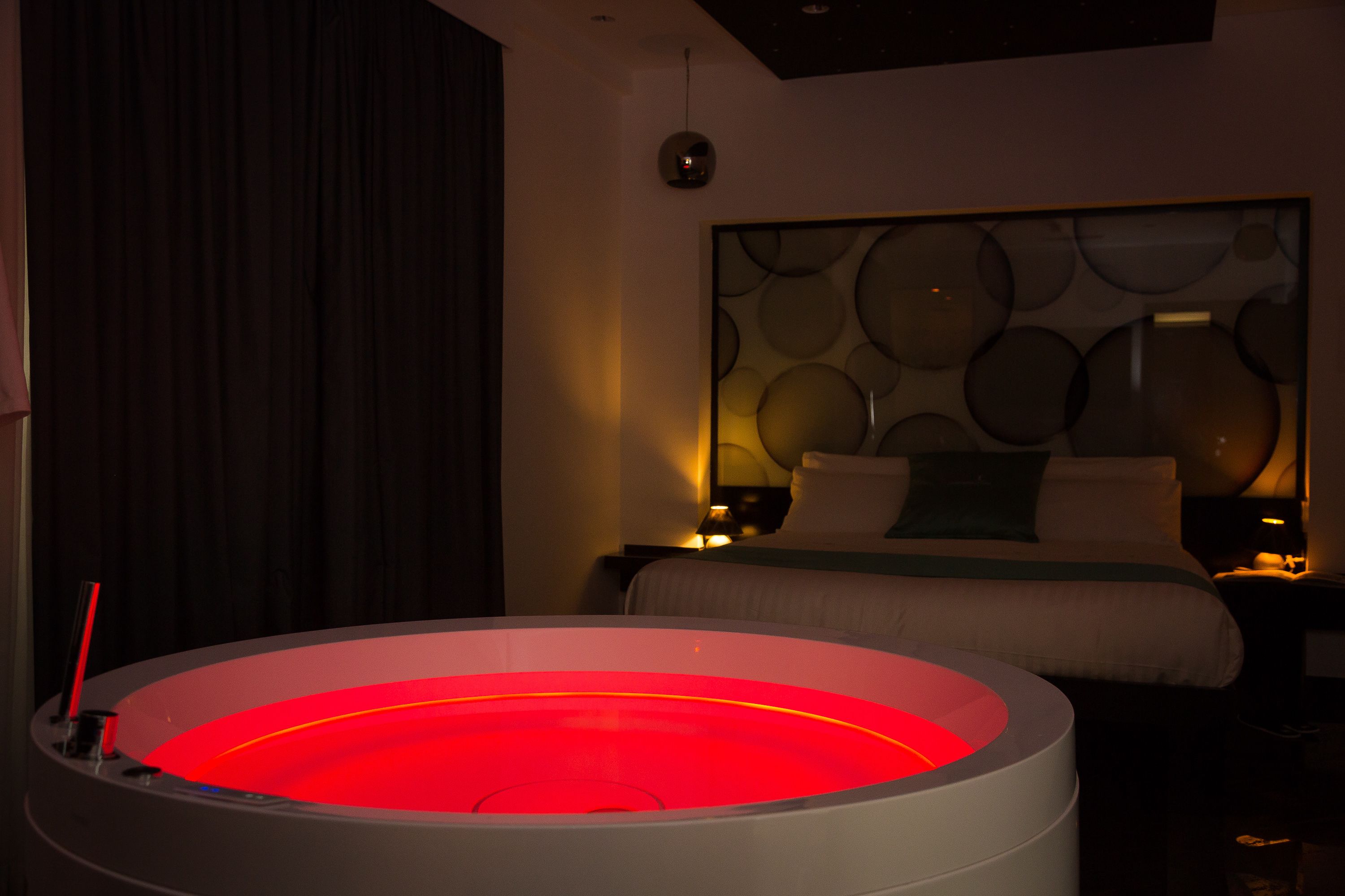 Ein modernes Hotelzimmer mit einer runden, beheizten Bodenfläche, einem großen Bett mit vielen Kissen und einer Wand mit kreisförmigen Mustern.