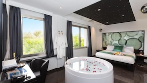 A modern hotel room with a large bed, a sitting area with a desk, a bathtub, and a view of greenery outside. - JC Hotel (Rome)
