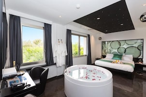 Camera d'albergo moderna con un letto grande, un'area salotto con scrivania, una vasca da bagno e vista sul verde.