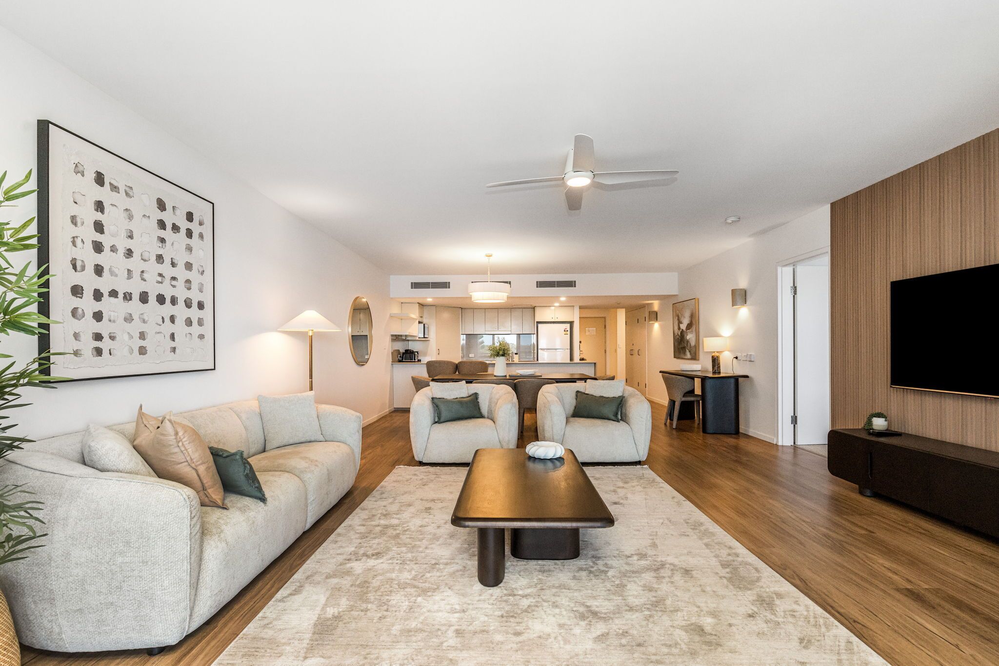 A modern living room with a sofa, coffee table, and a TV. There is a kitchen in the background.