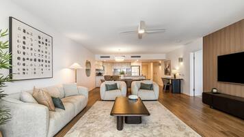 A modern living room with a sofa, coffee table, and a TV. There is a kitchen in the background.