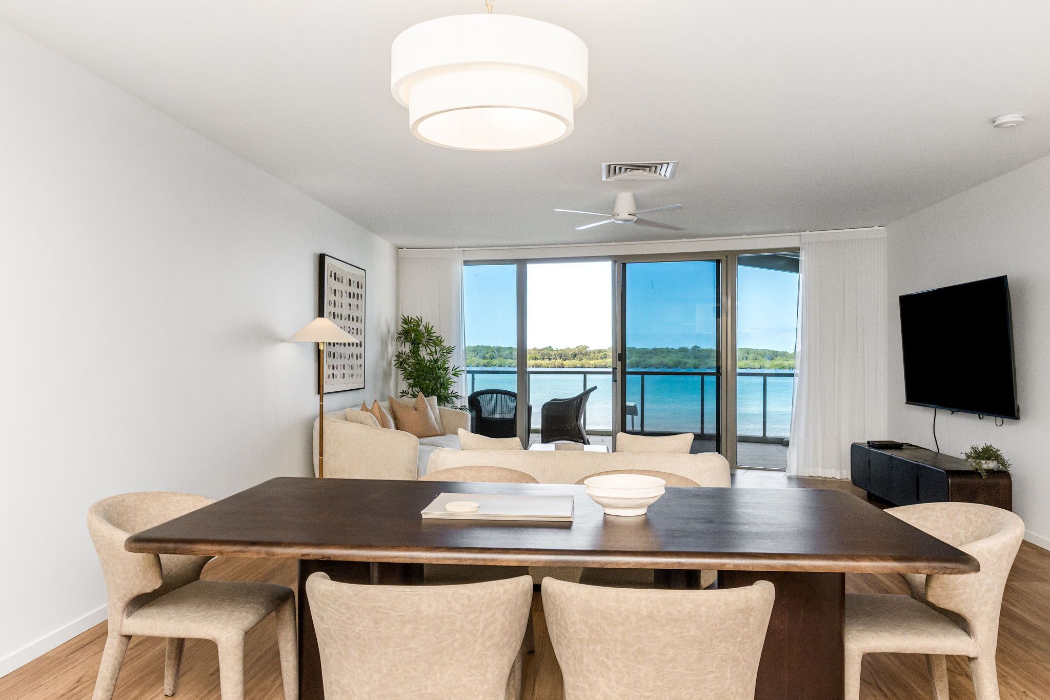 Una sala de estar moderna con una gran mesa de comedor, asientos cómodos, un televisor de pantalla plana y un balcón con vista al agua.