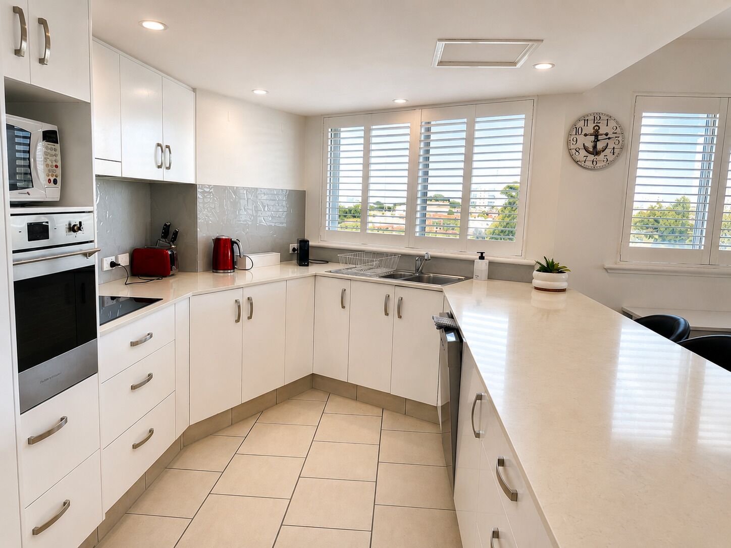 Una cocina moderna con armarios blancos, horno empotrado, cafetera y lavabo.