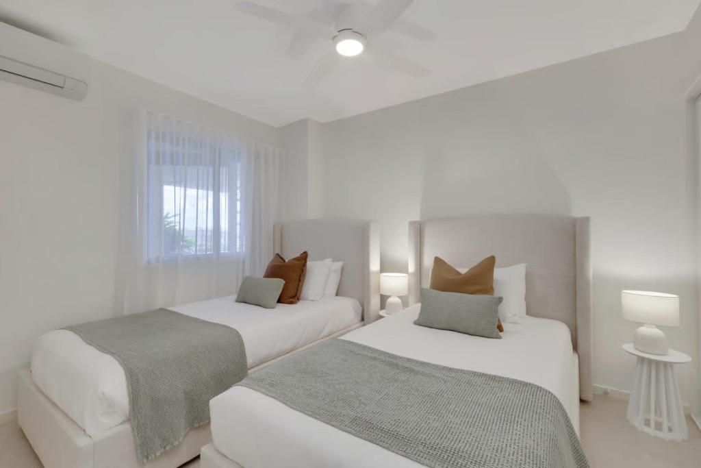 A hotel room with two beds, a ceiling fan, and a window with sheer curtains.
