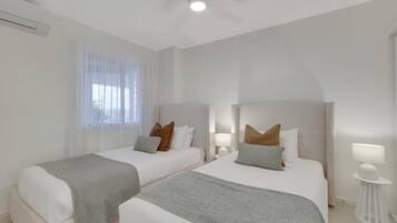 A hotel room with two beds, a ceiling fan, and a window with sheer curtains.