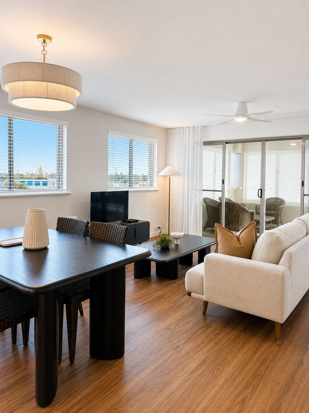 A modern living room with a dining area, large windows, and a view of the cityscape.