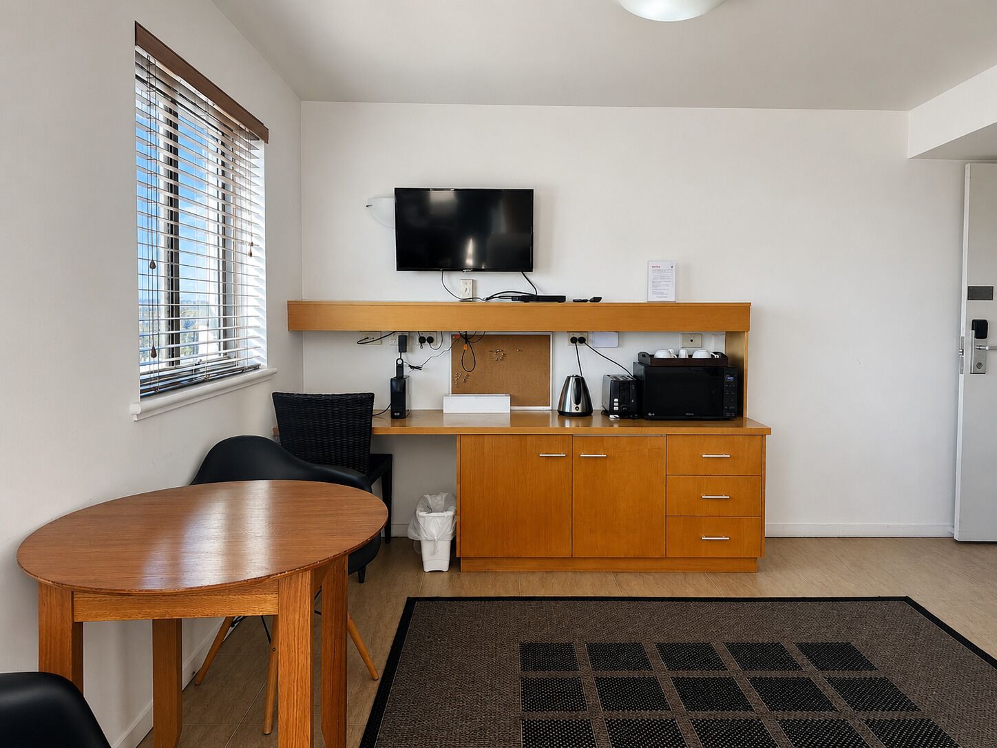 A compact kitchenette with a flat-screen TV, a microwave, a kettle, and a toaster on a wooden countertop.