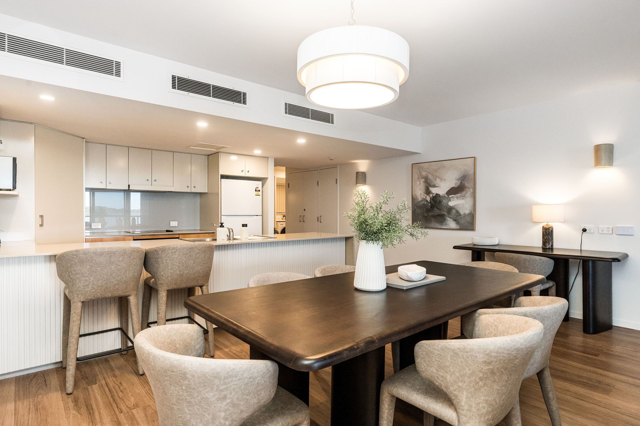 Una cocina moderna con armarios blancos, una mesa de comedor de madera y un florero con plantas.