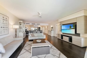 A modern living room with a flat-screen TV, a sofa, a coffee table, and a ceiling fan.